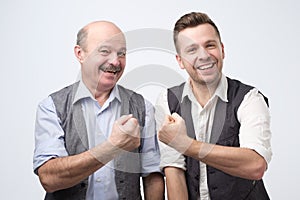 Two happy buddies wearing shirt and vest smiling and showing fis