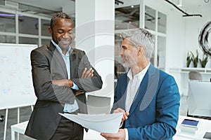 Two happy businessmen talking about deal standing in meeting room in modern office