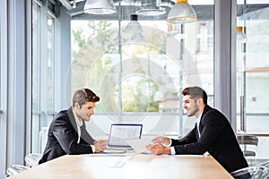 Two happy businessmen working together using laptop on business meeting