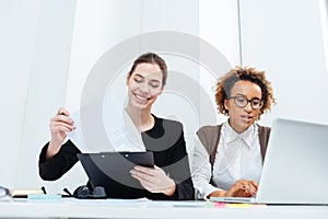 Two happy businesswomen using clipboard and laptop together