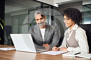 Two happy busy diverse business people talking using laptop working in office.