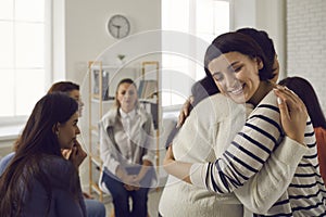 Smiling young women embracing each other in support group meeting or therapy session