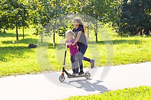 Two happy caucasian kid girls having fun riding on a cick scooter in a park in summer
