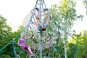 Two happy caucasian kids having fun on playground, climbing the rope net