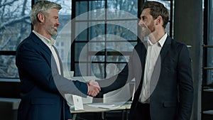 Two happy caucasian men businessmen talking in office shake hands after successful negotiations man seller handshake
