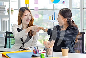 Two happy cheerful Asian millennial professional successful female businesswomen in formal suit sitting together holding hands