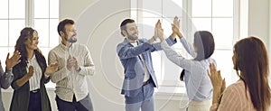 Two happy business people give each other a high five while coworkers are applauding