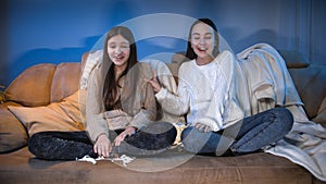 Two happy cheerful girls laughing and having fun while watching comedy movie at night