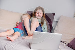 Two happy children a boy and a girl lie on a sofa in home clothes and watch video on a laptop