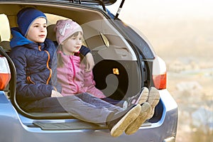 Two happy children boy and girl sitting together in a car trunk. Cheerful brother and sister hugging each other in family vehicle