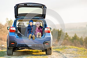 Two happy children boy and girl sitting together in a car trunk. Cheerful brother and sister hugging each other in family vehicle