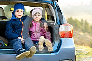 Two happy children boy and girl sitting together in a car trunk. Cheerful brother and sister hugging each other in family vehicle