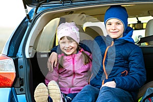 Two happy children boy and girl sitting together in a car trunk. Cheerful brother and sister hugging each other in family vehicle