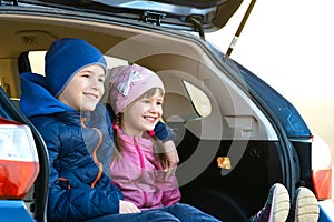 Two happy children boy and girl sitting together in a car trunk. Cheerful brother and sister hugging each other in family vehicle