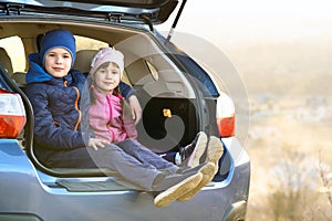 Two happy children boy and girl sitting together in a car trunk. Cheerful brother and sister hugging each other in family vehicle