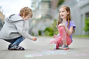 Two happy children drawing with colorful chalks on a sidewalk. Summer activity for small kids.