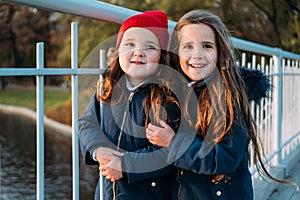 Two happy children hugging in autumn park. Close up sunny lifestyle fashion portrait of two beautiful caucasian girls outdoors,wea