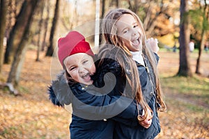Two happy children hugging in autumn park, smiling, looking at camera. Cute stylish children wearing trendy outfit in navy and red