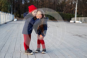 Two happy children hugging and kissing in autumn park. Close up sunny lifestyle fashion portrait of two beautiful caucasian girls