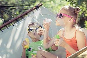 Two happy children lie on a hammock and play with soap bubbles