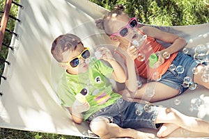 Two happy children lie on a hammock and play with soap bubbles