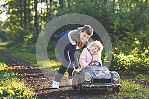 Two happy children playing with big old toy car in autumn forest, outdoors. Kid boy pushing and driving car with little