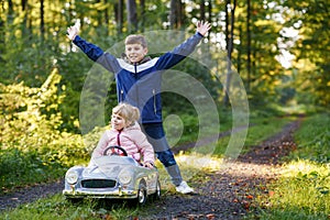 Two happy children playing with big old toy car in autumn forest, outdoors. Kid boy pushing and driving car with little