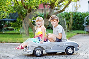 Two happy children playing with big old toy car in summer garden, outdoors. Kid boy pushing and driving car with little