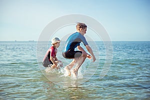 Two happy children playing and jumping in water in neoprene suits in Baltic sea