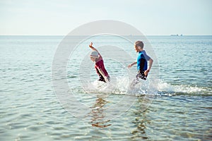 Two happy children playing and jumping in water in neoprene suits in Baltic sea