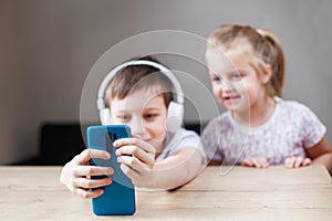 two happy children playing on the smartphone in headphones. people  children and technology concept