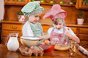 Two happy children preparing eggs for cookies in the kitchen