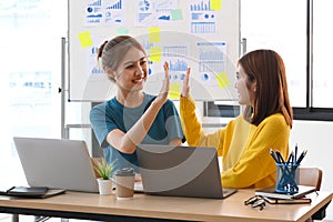 Two happy colleagues are giving high fives each other to celebrate corporate success.