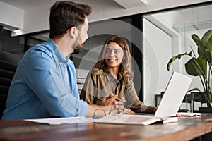 Two happy colleagues professional man and woman talking at work with laptop.