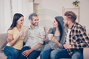 Two happy couples sitting on cozy sofa at home, having nice conversation and embracing. A weekend with best friends, what can be