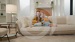 Two happy cute caucasian little kids girls friends children reading book read fairy tale in living room cozy sofa having