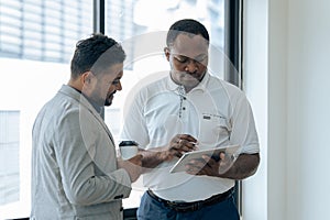 Two happy diverse coworker discussing report financial on tablet, working on project together