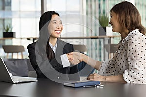 Two happy diverse office colleague women shaking hands, laughing