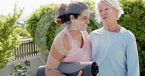 Two happy diverse senior women with exercise mats, embracing and smiling in garden, slow motion