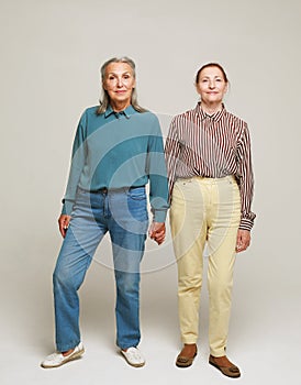 Two happy elderly women friends on grey background. Full length portrait.