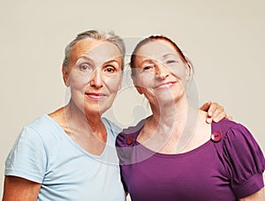 Two happy elderly women friends hugging on grey background.