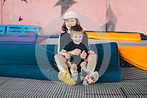 Two happy emotions children, brothers playing and having fun while jumping on bouncing trampoline in playground in summer. Hug,