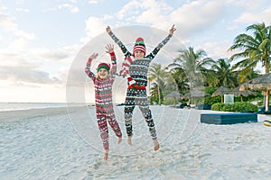 Two happy excited children jumping on sandy beach in Christmas pyjamas
