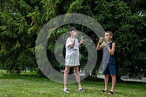 Two happy fair-haired children girl and boy making soap bubbles and playing together in nature outdoors in the park