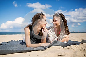 Two happy female friends lying on beach talking