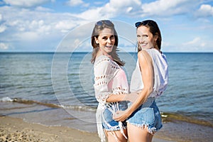 Two happy female friends standing together on beach