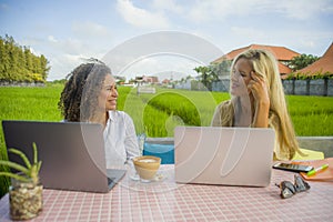 Two happy female friends working outdoors at beautiful internet cafe with laptop computer caucasian woman and an afro mixed girl