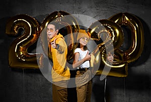 Two happy friends boy and a girl are celebrating a new year partywith ballonss numbers 2020 on a concrete background.