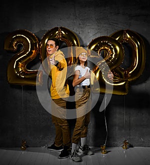 Two happy friends boy and a girl are celebrating a new year partywith ballonss numbers 2020 on a concrete background.