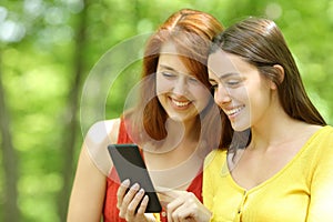 Two happy friends checking smart phone in a park